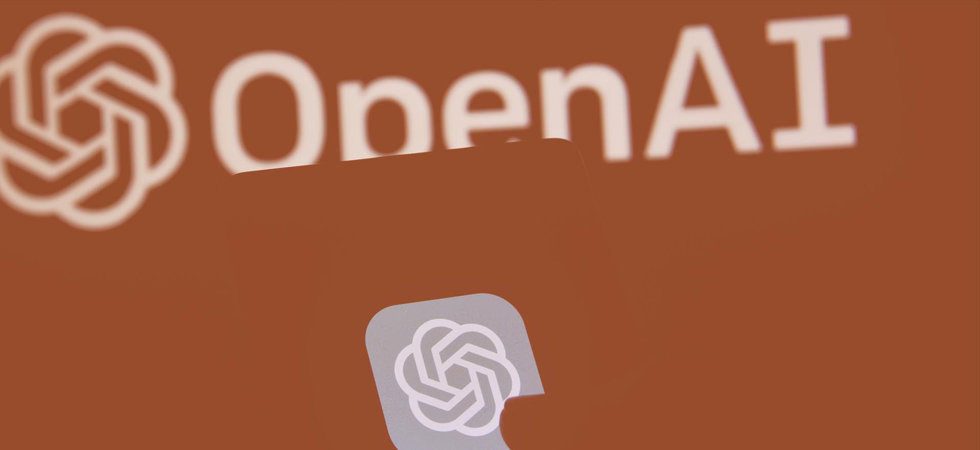 Mobile phone with OpenAI logo infront of big OpenAI logo
