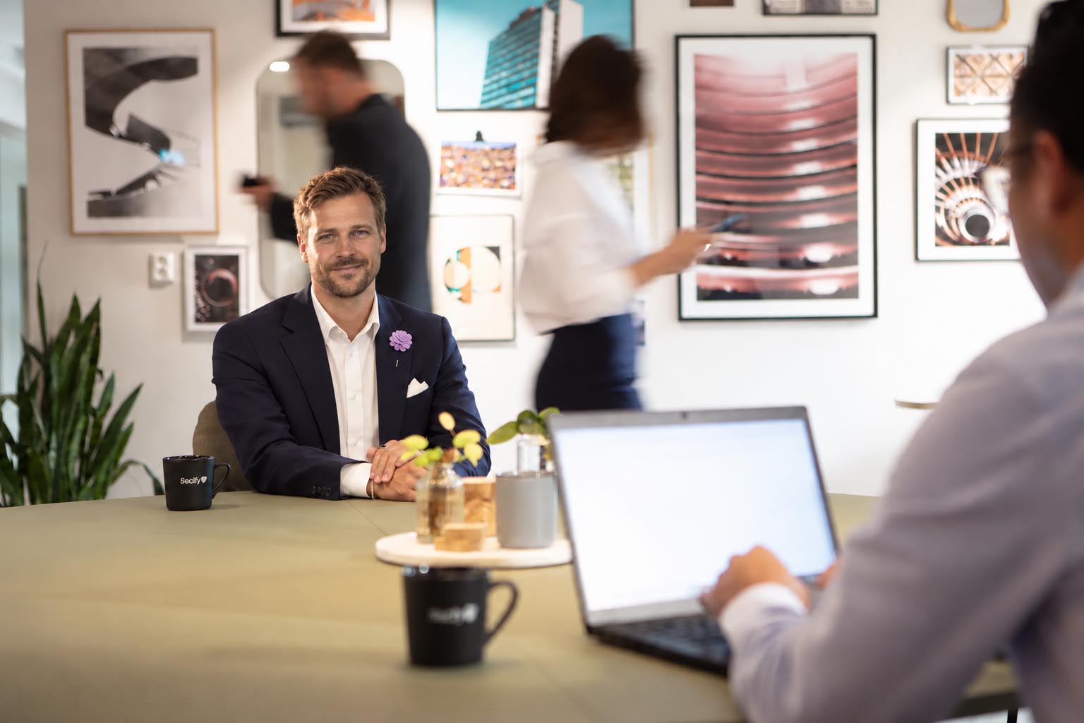 olof-inmotion Två personer sitter vid ett bord. En person bakom en dator samtalar med person framför datorn