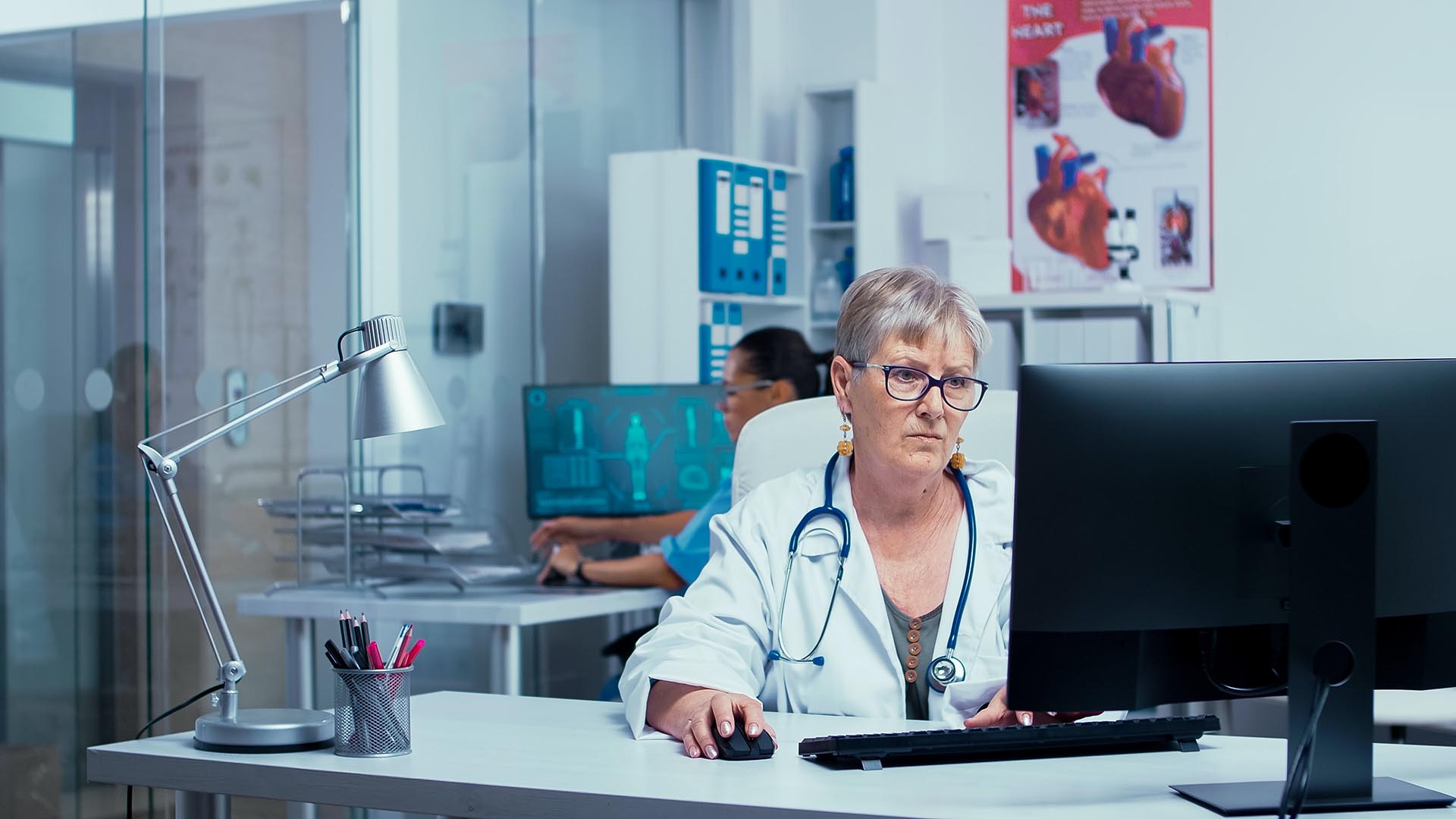 Sjuksyster eller läkare som sitter ner bakom en datorskärm och arbetar med datorn