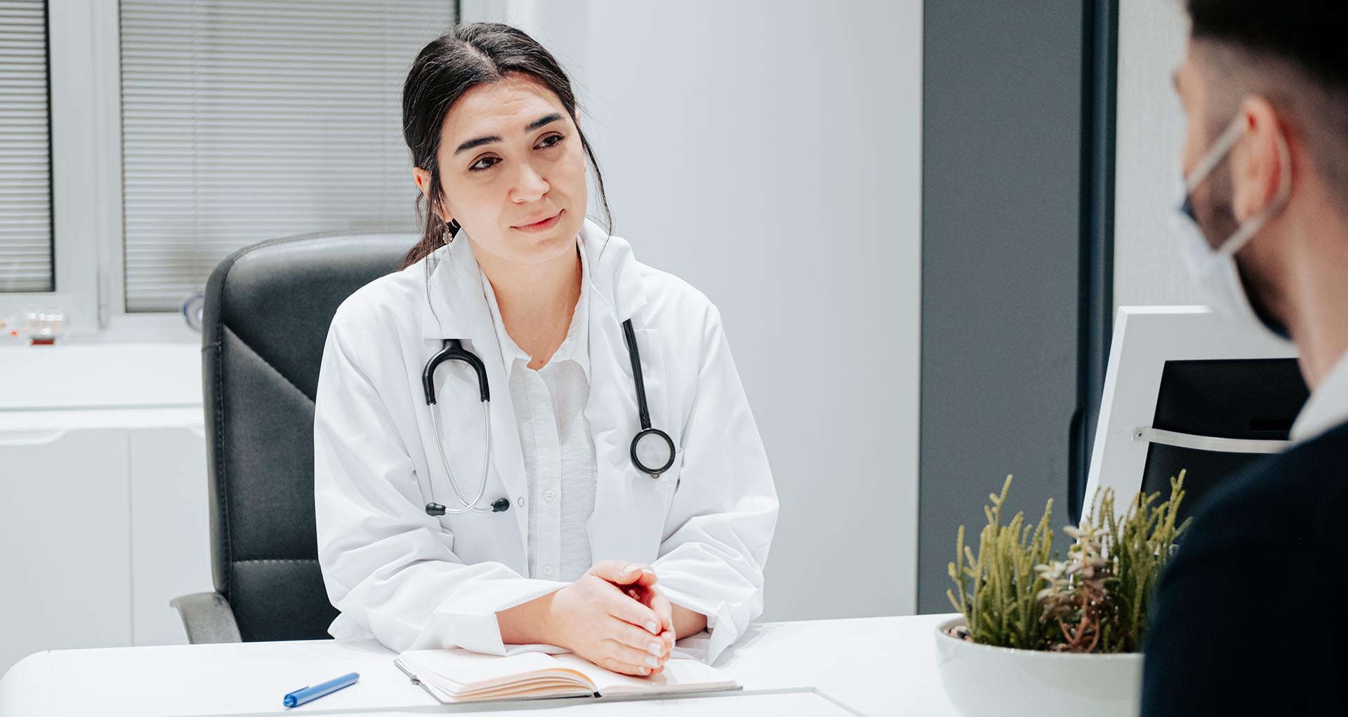 Kvinnlig läkare sitter vid ett skrivbord och samtalar med en patient
