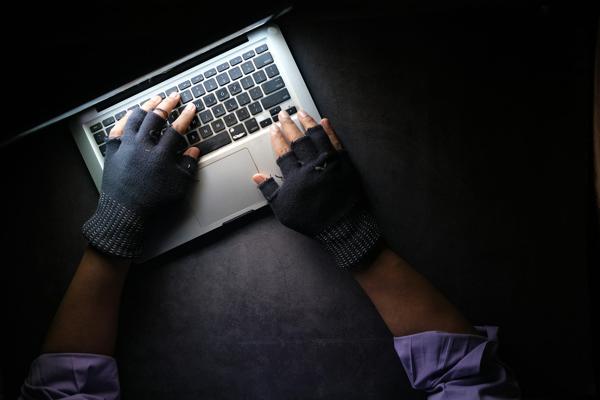Händer som bär fingervantar och skriver på laptop