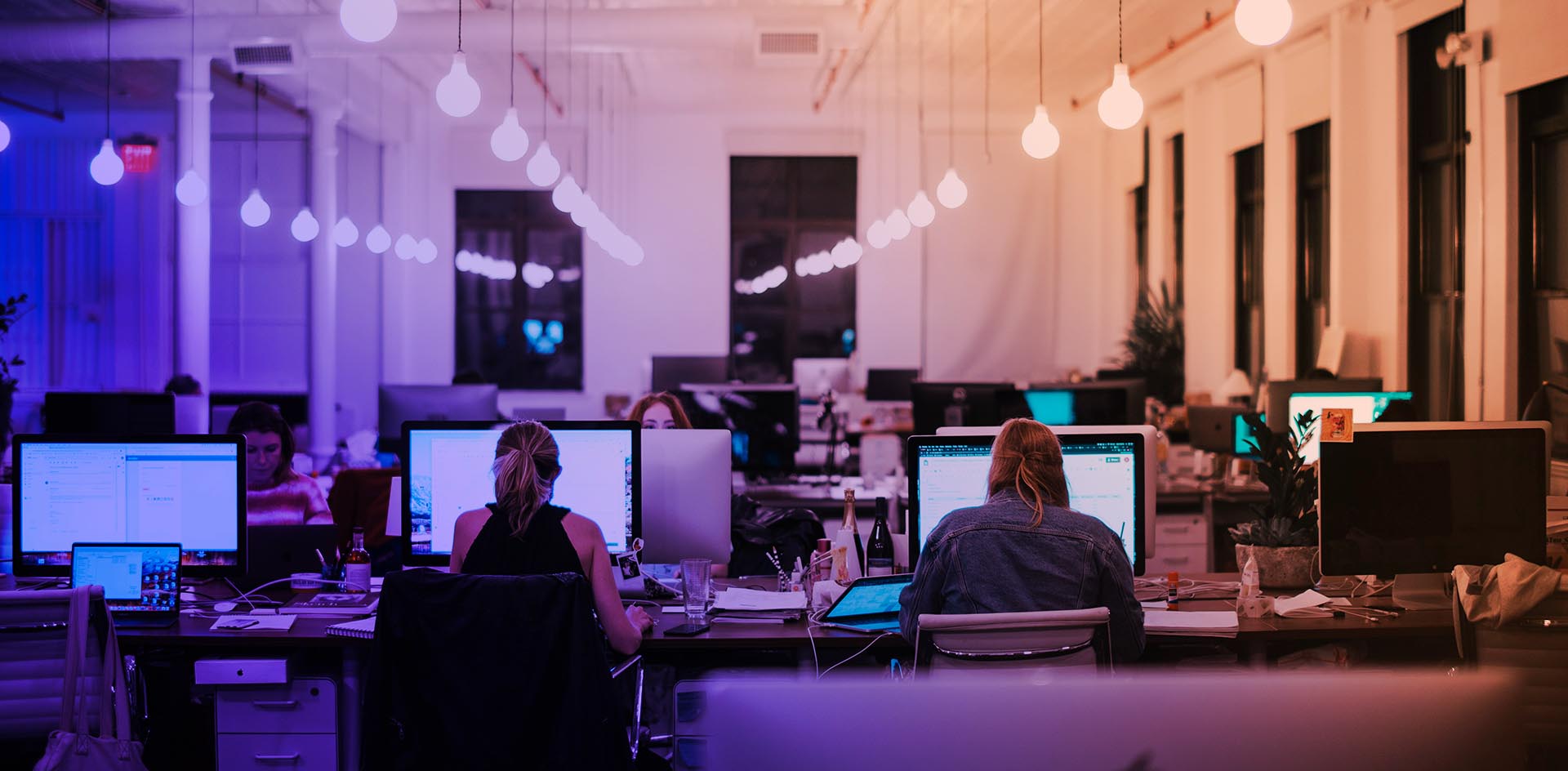 En blå-orange tonad bild på ett kontorslandskap med datorer och personer vid datorerna