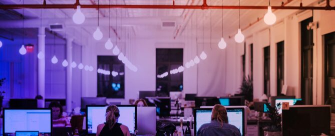 En blå-orange tonad bild på ett kontorslandskap med datorer och personer vid datorerna