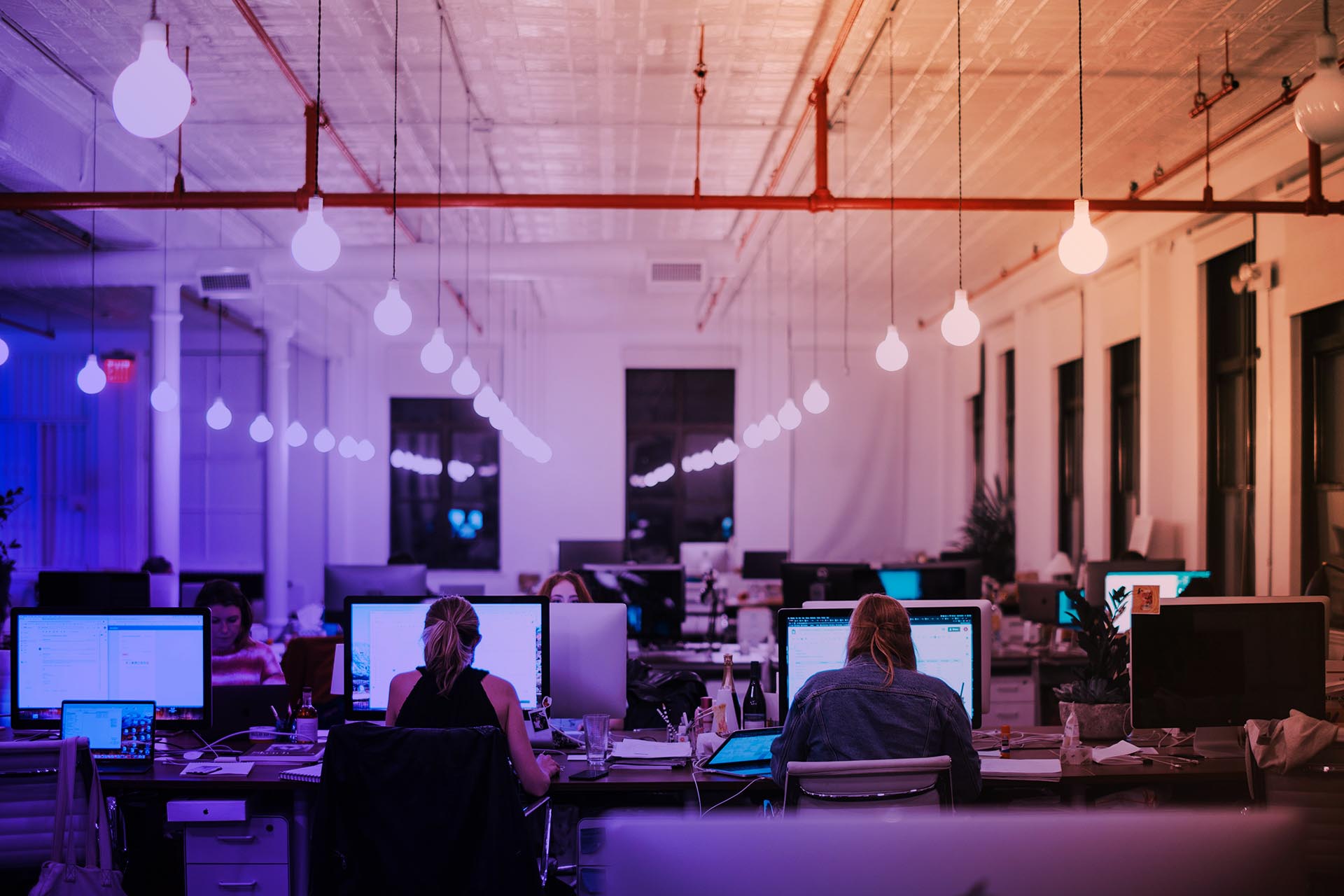 En blå-orange tonad bild på ett kontorslandskap med datorer och personer vid datorerna