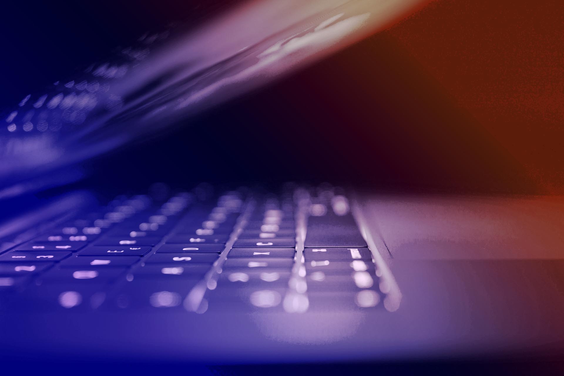 Bild på en bärbar dator som nästan är stängd. Bilden har en ton som går från blått till orange